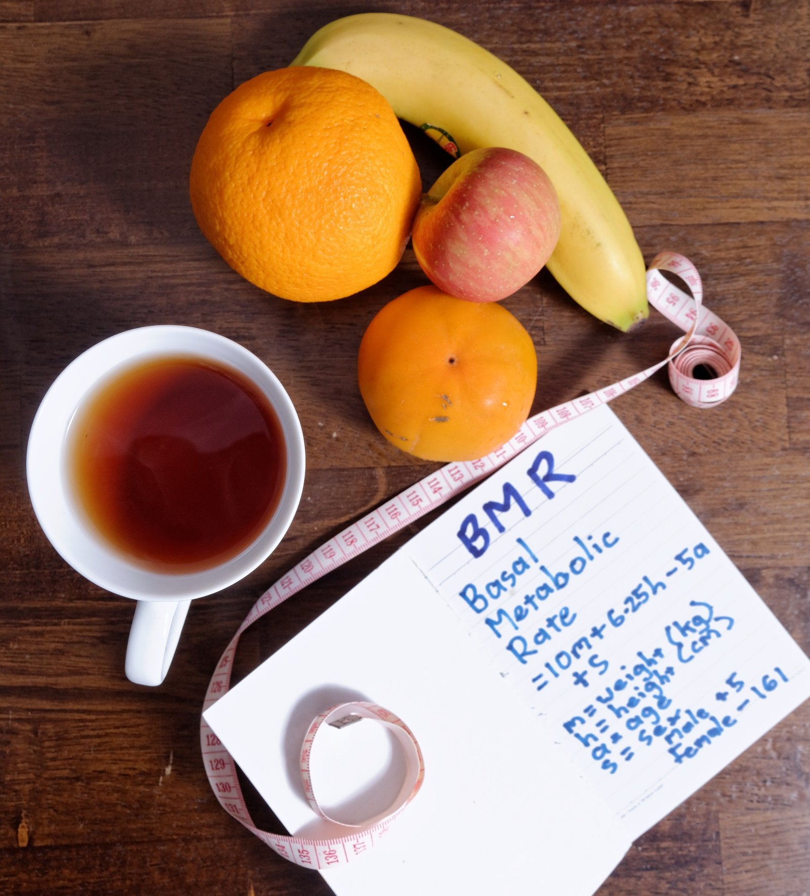 foto still life di tavolo con sopra una tazza con tisana, frutta un metro da sarta e un blocco con appunti sul Metabolismo basale . Concetto di motivazione per sport e dieta 