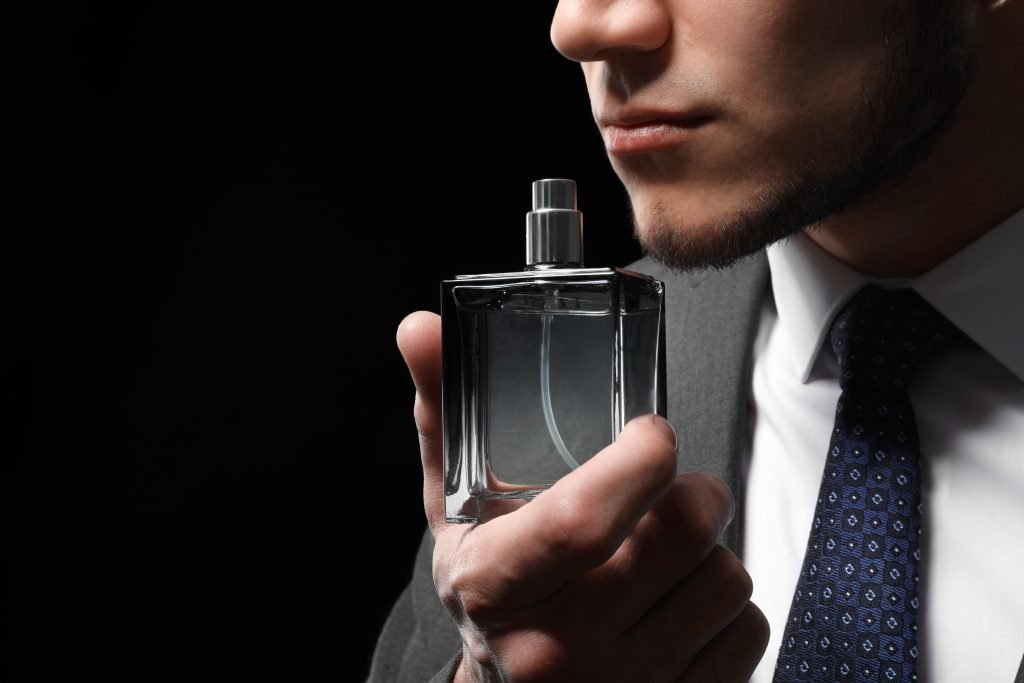 uomo di bell'aspetto in abito scuro con una boccetta di profumo con sfondo nero.Primo piano tema Profumi migliori da regalare a lui per San Valentino