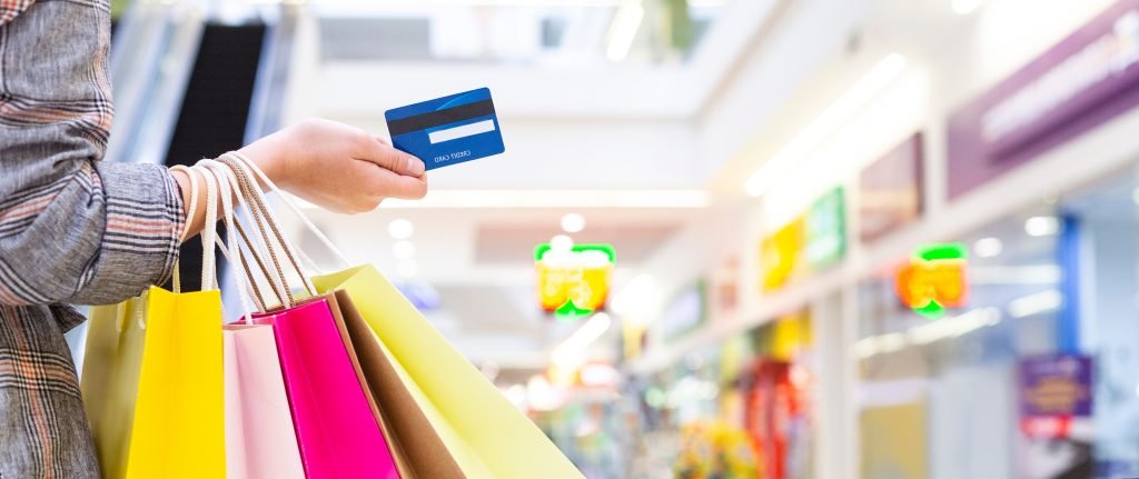 DONNA CHE TIENE IN MANO UNA CARTA DI CREDITO E DEI SACCHETTI DELLO SHOPPING IN UNO SFONDO DI UN NEGOZIO 