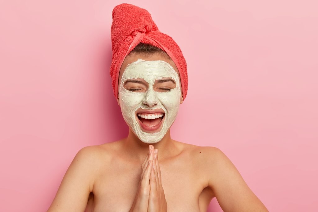 ragazza crema viso per l'estate sul viso come maschera e asciugamano rosso a turbante sulla testa sfondo rosa