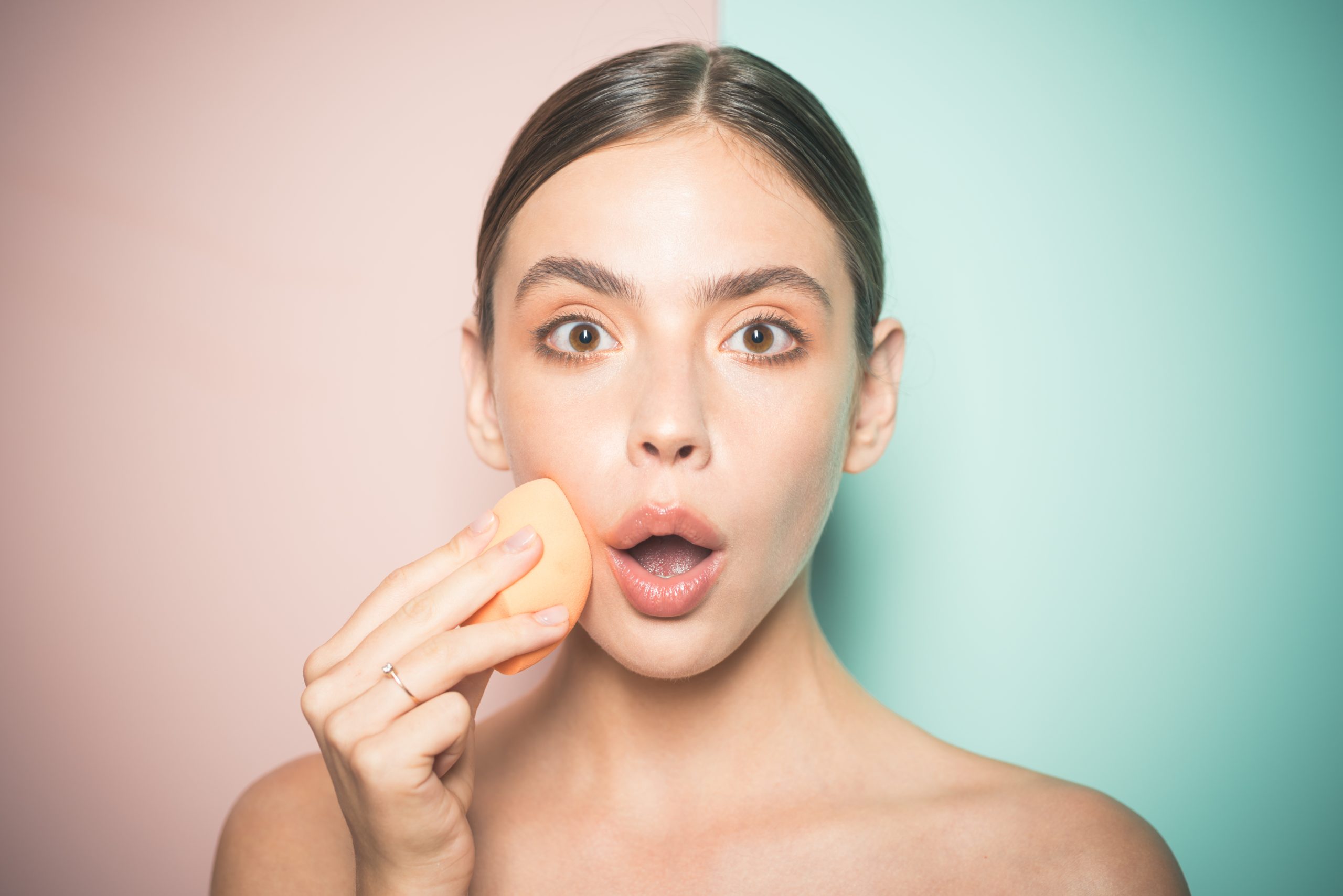 ragazza stupita si trucca con una spugnetta a forma di uovo per ottenere un look naturale e luminoso