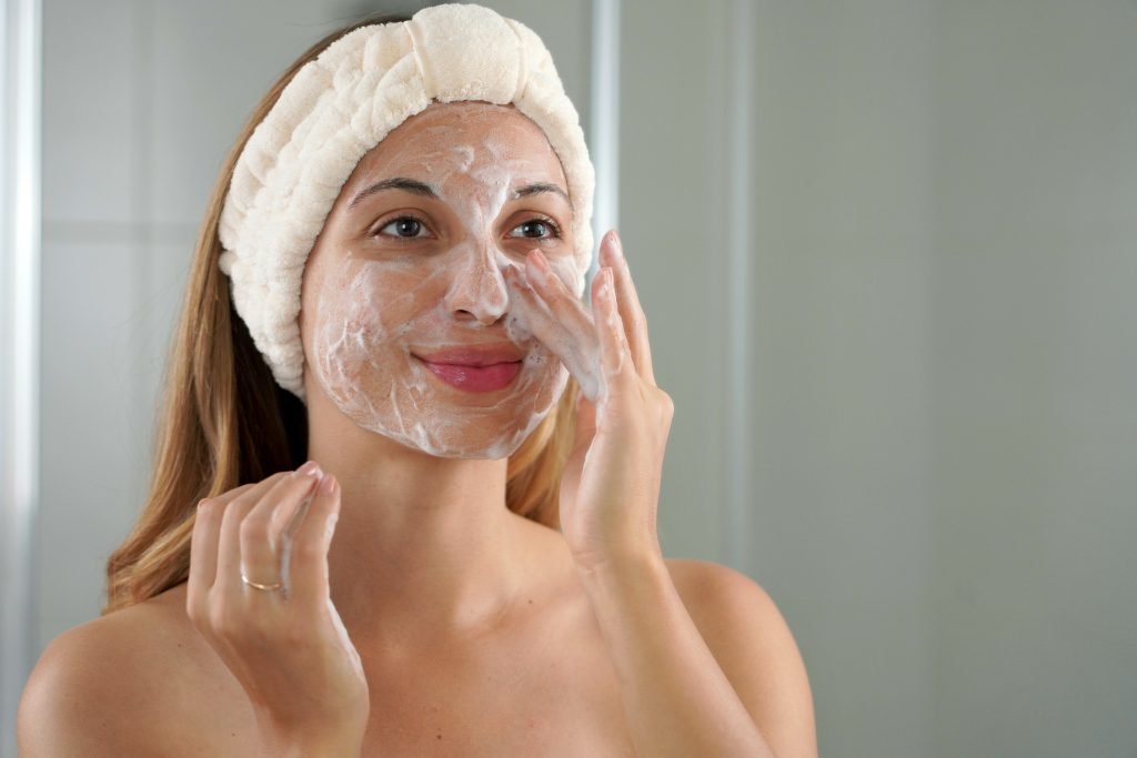 ragazza con fascia di spugna che deterge viso prima di mettere la crema viso per l'estate