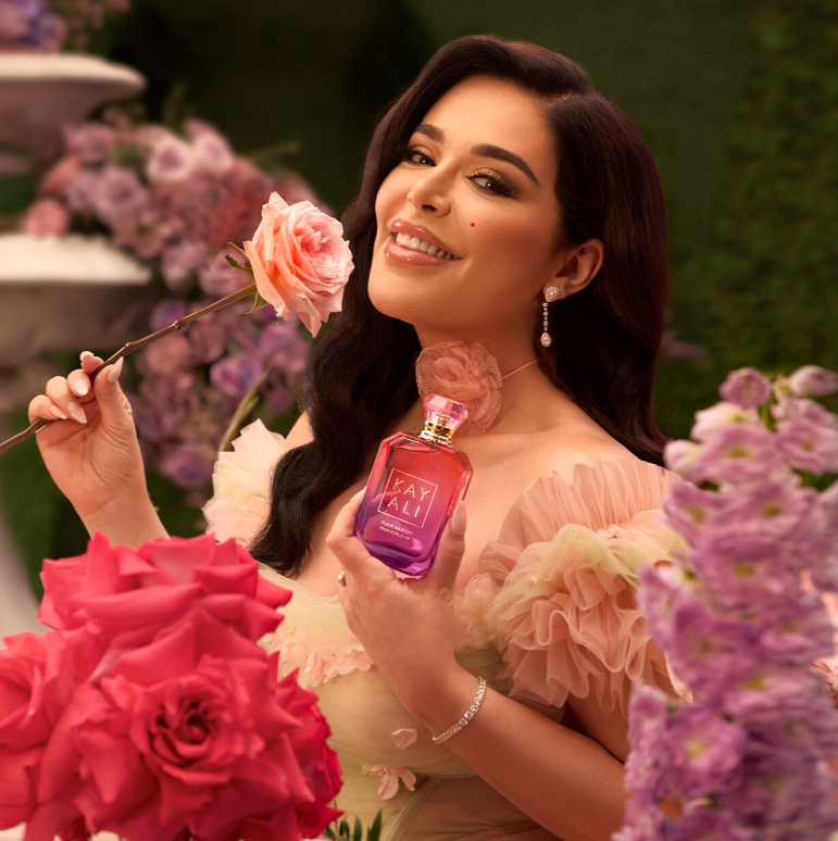 mona kattan fotgrafata con una rosa in un giardino di rose mentre mostra il suo profumo Kayali Fleur Majesty Rose Royale 31 – Eau de Parfum