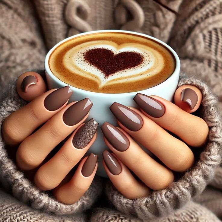 mani con le unghie smaltate con smalto mocha mousse che tengono una tazza con un cappuccino con la schiuma a forma di cuore