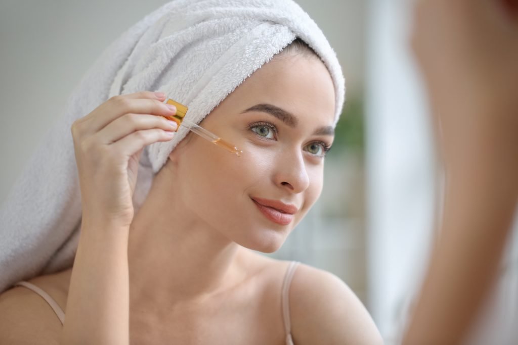 ragazza con asciugamano di spugna bianca che usa un siero per la pelle del viso prima di applicare la sua crema viso per l'estate