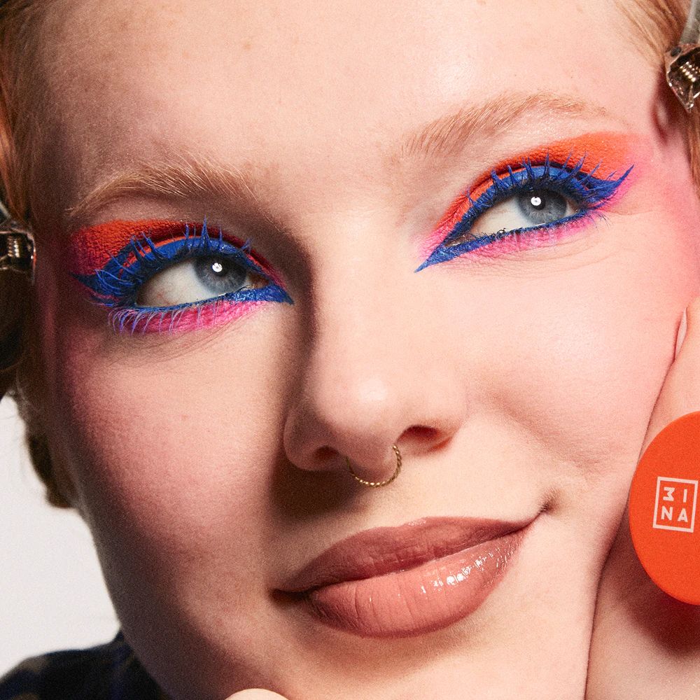 viso di ragazza con occhi verdi e capelli rossis che indossa mascara colorati 3ina e ne tiene uno in mano