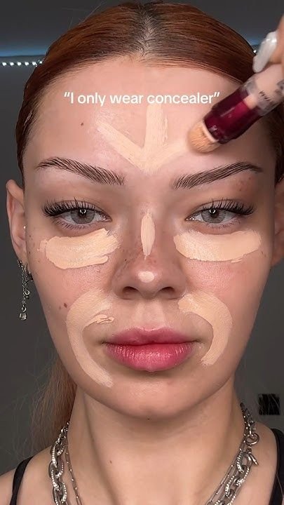 ragazza coi capelli rossi raccolti con la riga in mezzo usa il correttore maybelline cancella età per realizzare ua base viso naturale