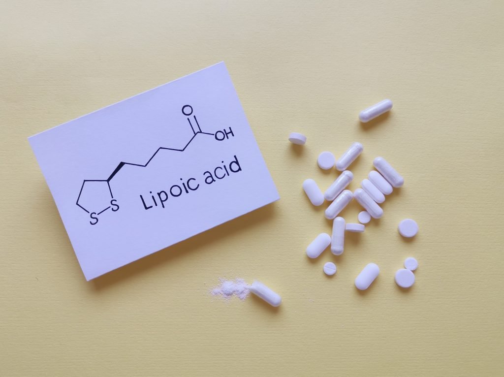 foglio su cui è scritta la formula chimica dell' acido alfa lipoico e alcune pastiglie accanto su sfondo beige