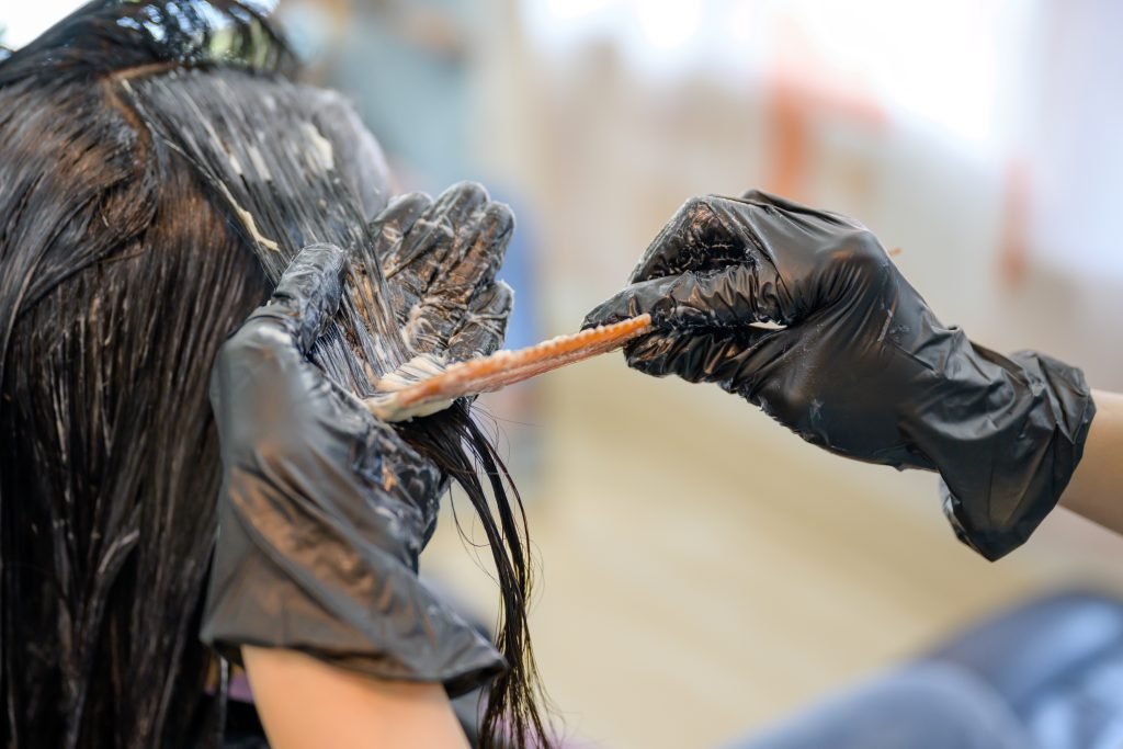 Parrucchiere con guanti neri che tinge i capelli di una giovane donna con i capelli neri in un salone di bellezza