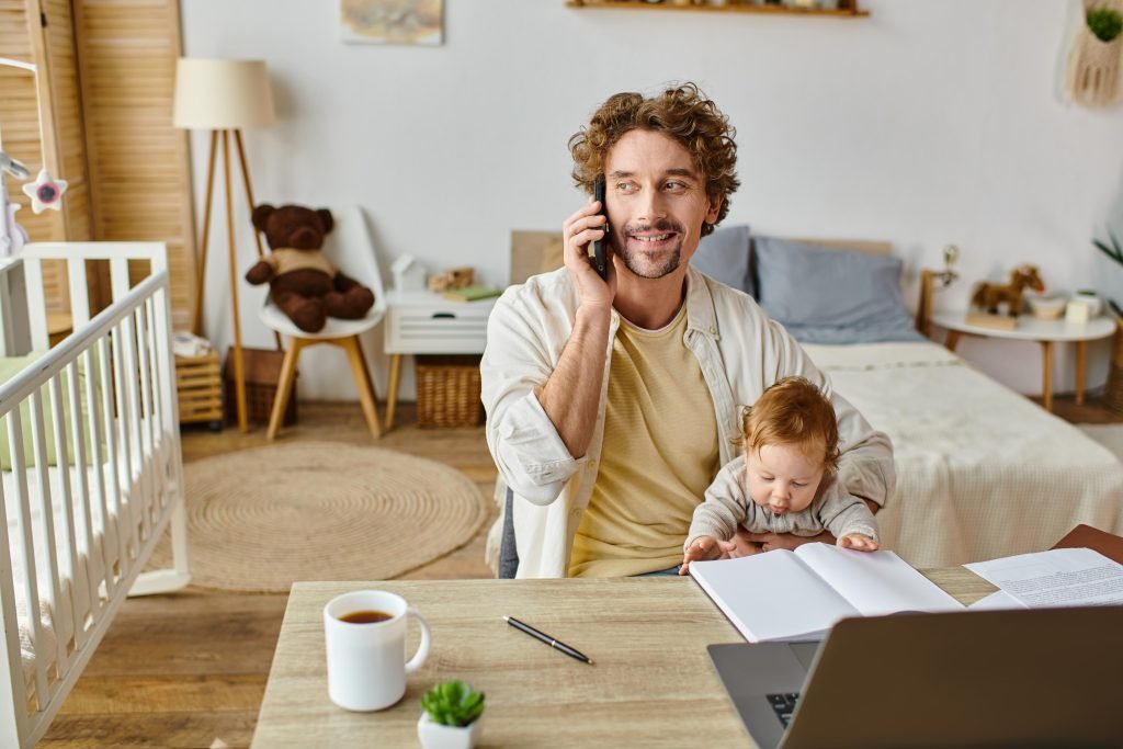 padre, con bimbo, che parla al telefono in un ambiente neutro e rilassante: concetto di come essere più produttivi se si dedica tempo agli affetti 