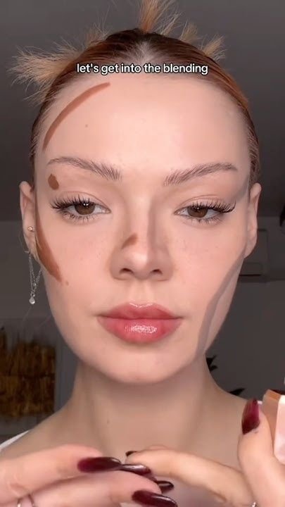 ragazza con i capelli raccolti che usa correttori scuri per realizzare il contouring su una base viso naturale