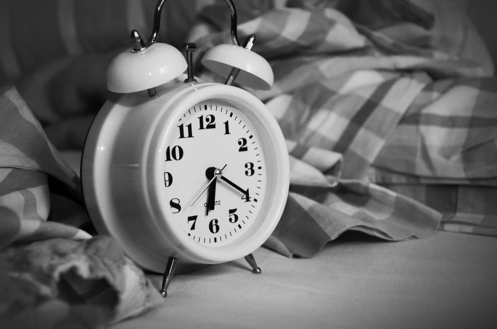 concetto di come essere più produttivi : primo piano di sveglia su letto che segna le 6.30 circa , immagine in bianco e nero 