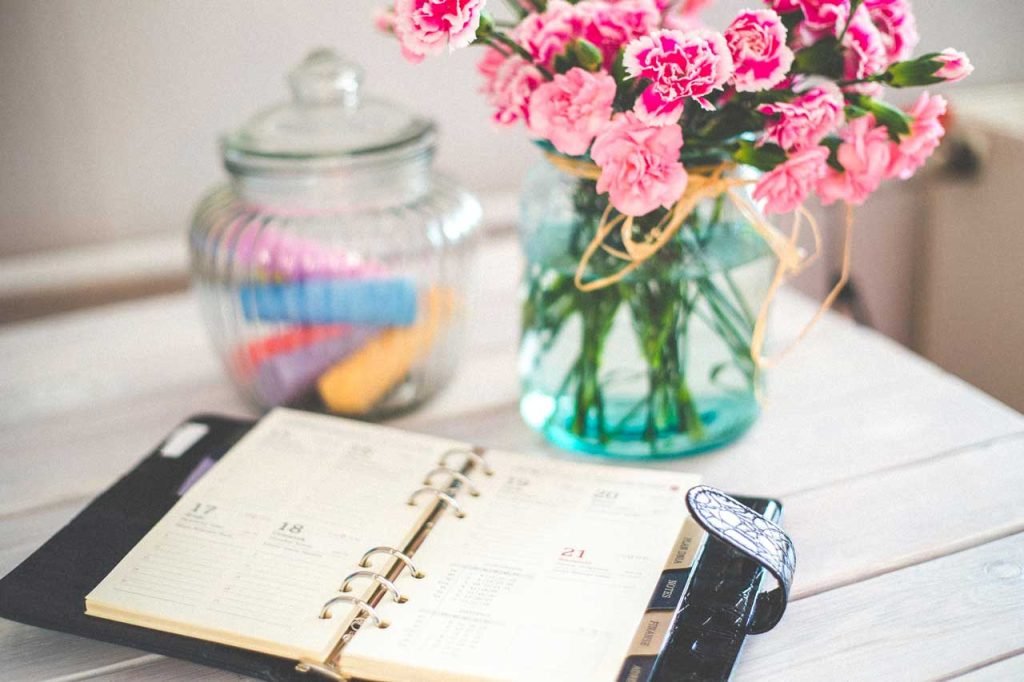 concetto del come essere produttivi : agenda aperta su sfondo con vaso di fiori 