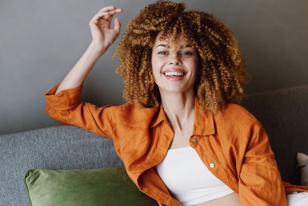 Modella afro con capello super riccio sorride felice e indossa una giacca arancione, mostrando emozioni di gioia e relax, 