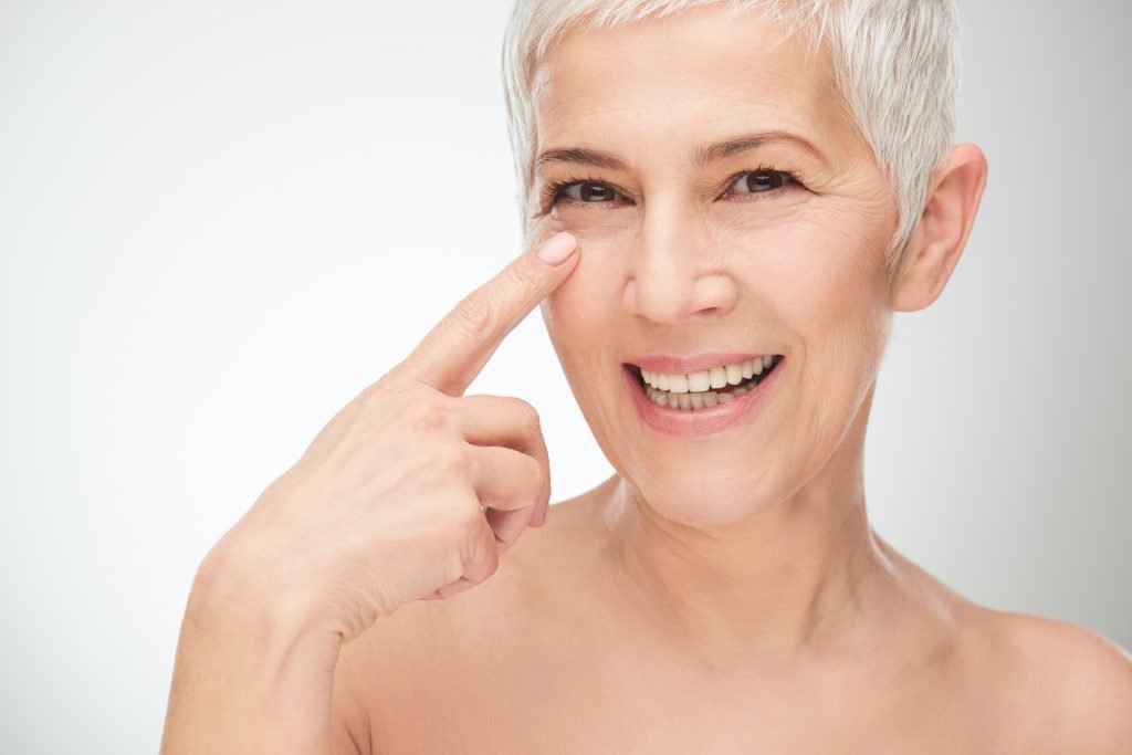 donna matura con capelli bianchi e corti in primo piano che indica il suo contorno occhi per il concetto di baking trucco per quale tipo di pelle è adatto?