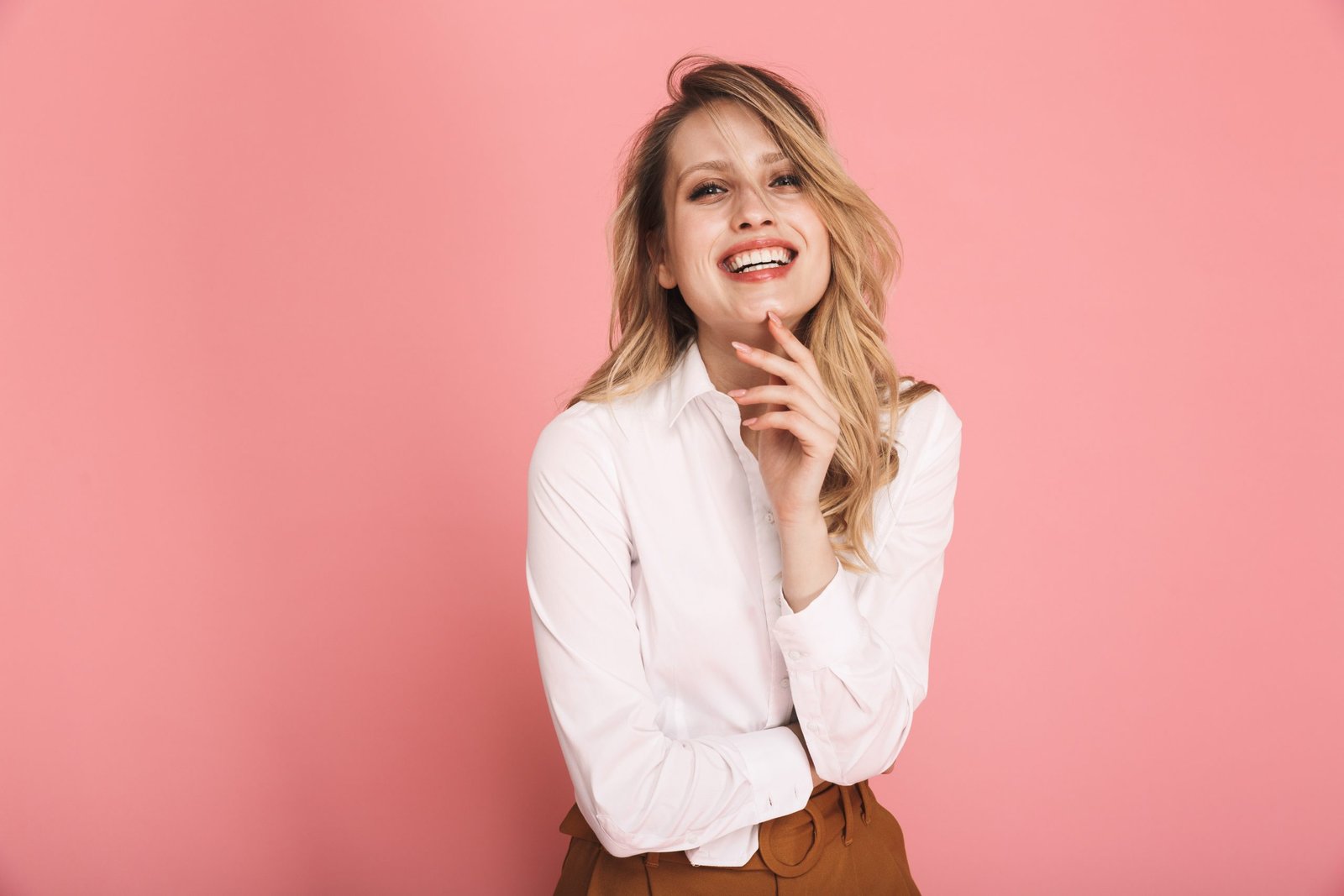 Ritratto di una splendida donnaCON BEI CAPELLI biondI sulla trentina, elegantemente vestita, sorridente e che guarda in camera, isolata su sfondo rosso. Concetto haircare, cura e integrazione con Biotina per capelli