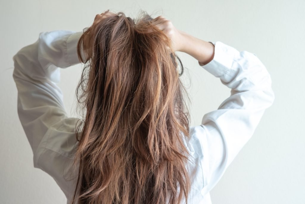 Vista posteriore una donna con problemi di capelli secchi e danneggiati, su sfondo semplice.