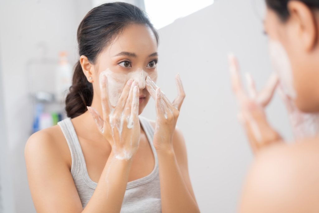  BELLA RAGAZZA ASIATICA LAVA IL VISO NEL SUO BAGNO DAVANTI ALLO SPECCHIO ESEGUENDO IL PRIMO PASSAGGIO DELLA DOPPIA DETERSIONE