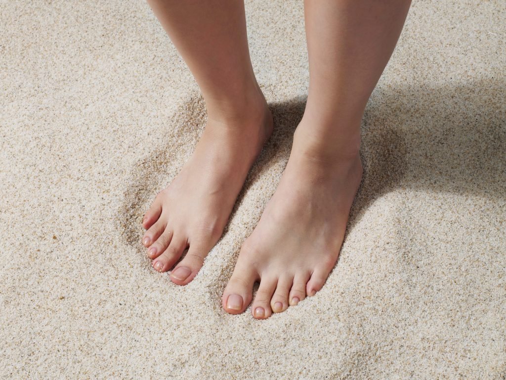 primo piano di piedi sulla sabbia - concetto della importanza di una pedicure fai da te per avere piedi curati in estate 