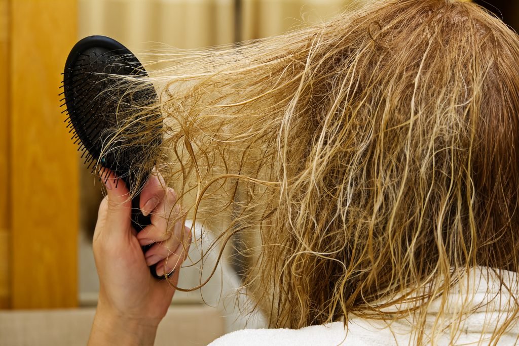 Giovane donna che si pettina i capelli arruffati dopo la doccia in un interno di un bagno, primo piano.