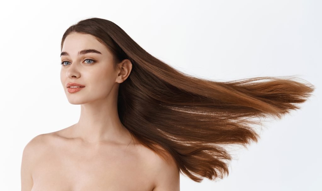 Ritratto di ragazza modella con lunghi capelli mossi. Glamour, bellissima donna bruna con sani e bellissimi capelli castani, isolata su sfondo bianco. Concetto di cura della pelle e bellezza dei capelli.