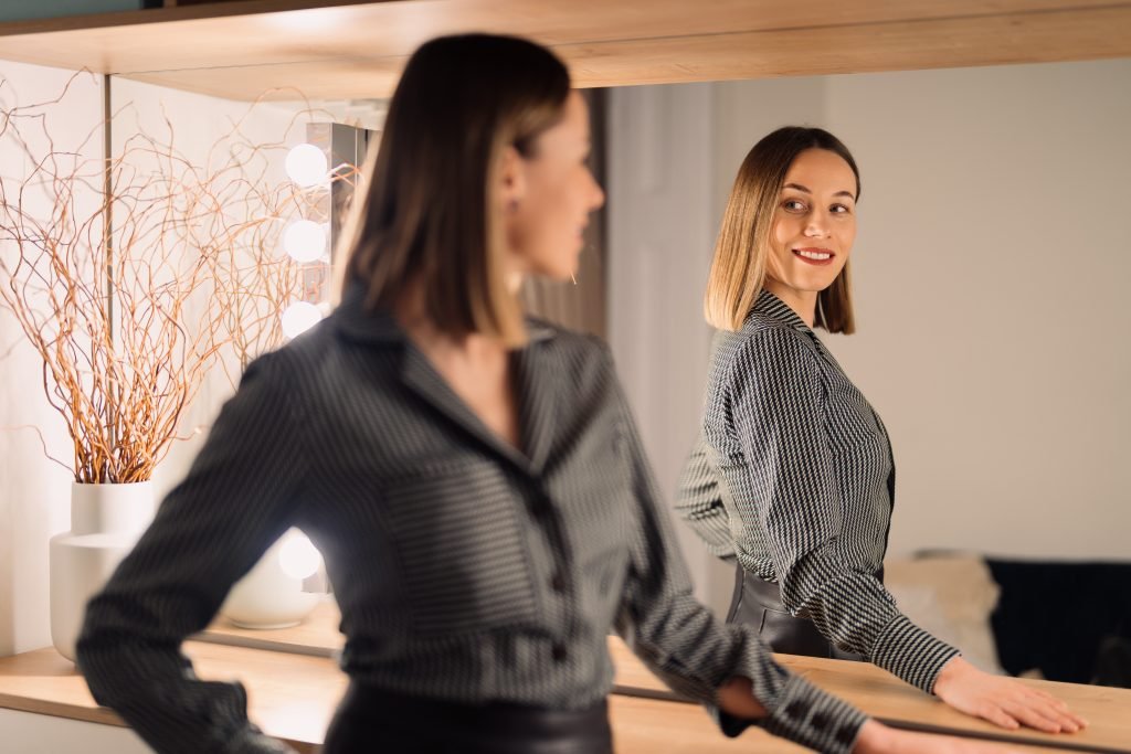 Donna sicura di sé che si guarda allo specchio in casa. Bellissimo design d'interni. concetto di cura di sé