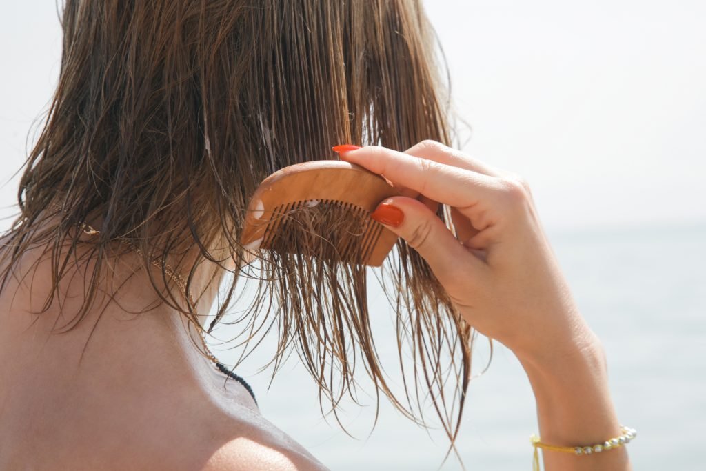 primo piano di spalle di donna che pettina i capelli al mare