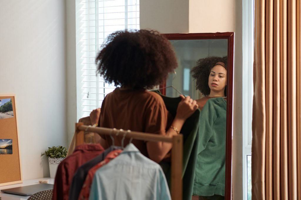 Una donna prova i vestiti davanti allo specchio per decidere cosa indossare - concetto di cura di sé