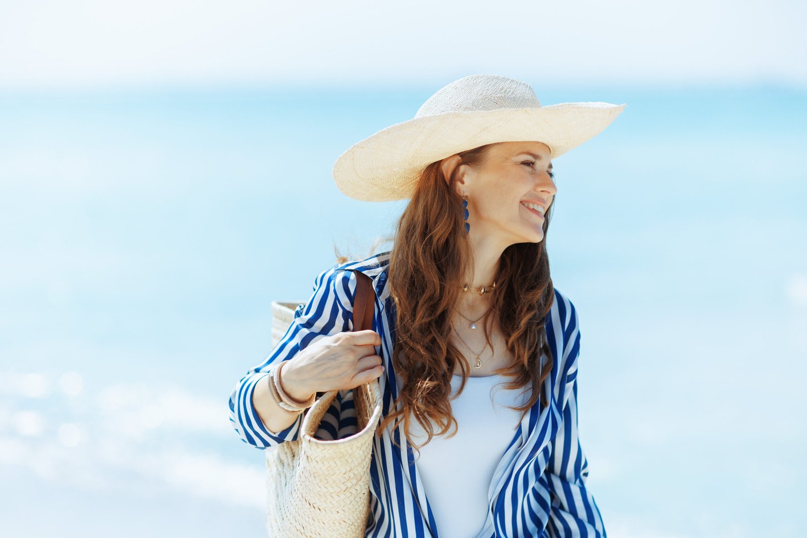 Felice donna moderna di 40 anni sulla costa oceanica con borsa e cappello di paglia - borse mare grandi ed economiche