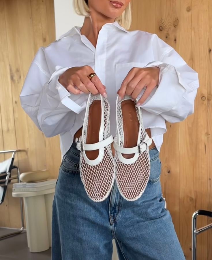 giovane ragazza bionda con camicia bianca e jeans che tiene in mano e mostra le ballerine bianche in rete economiche dupe di Alaia 