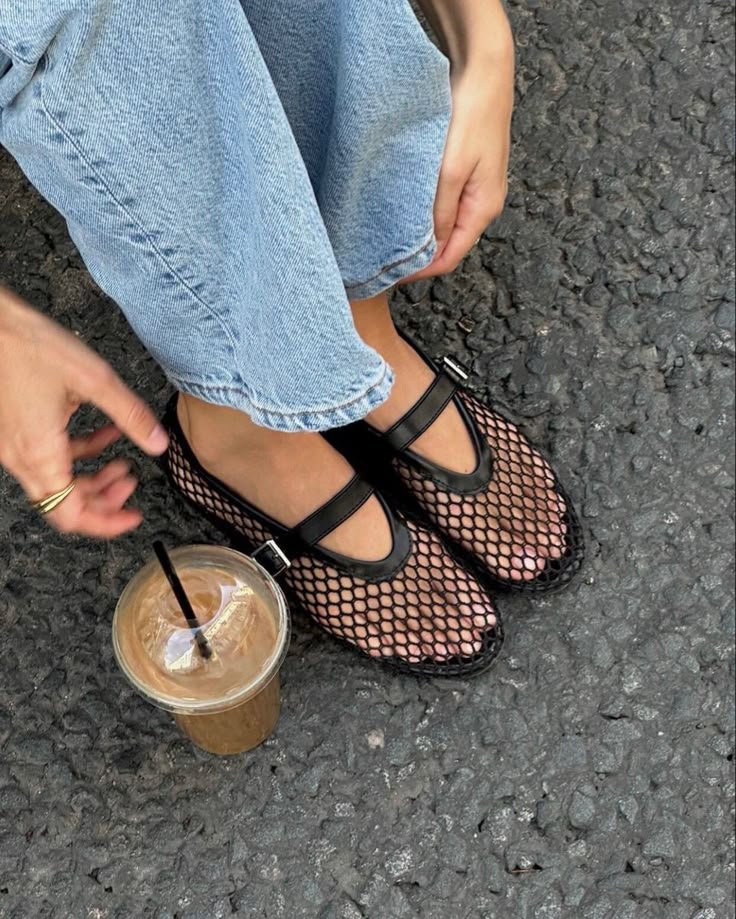 primo piano di piedi di donna seduta per terra con bibita con cannuccia accanto, che indossa le ballerine in rete di Alaia 
