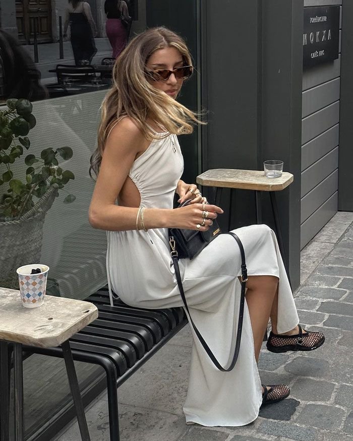 ragazza seduta fuori da un bar con abito lungo bianco e ballerine in rete economiche 