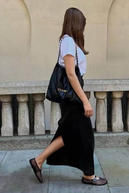 ragazza che passeggia per strada con tshirt bianca e gonna longuette nera e ballerine in rete economiche 