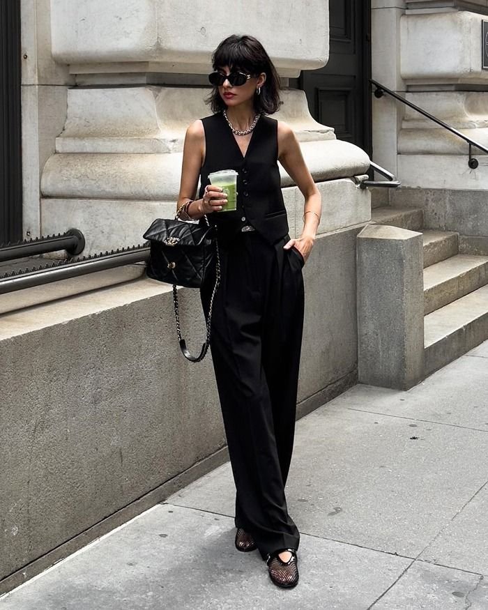 donna per strada con in mano una bibita con cannuccia vestita di nero con ballerine in rete Alaia 