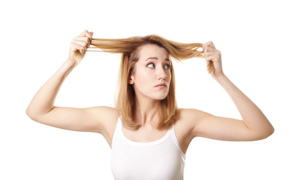 ragazza che tiene in mano le cicocche dei suoi capelli secchi e danneggiati su sfondo bianco per il concetto di Come curare i capelli