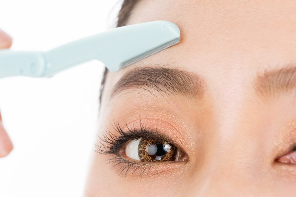 close up su occhio e sopracciglio di donna che fa dermaplaning con rasoio sopra il sopracciglio . Concetto di dermplaning pro e contro