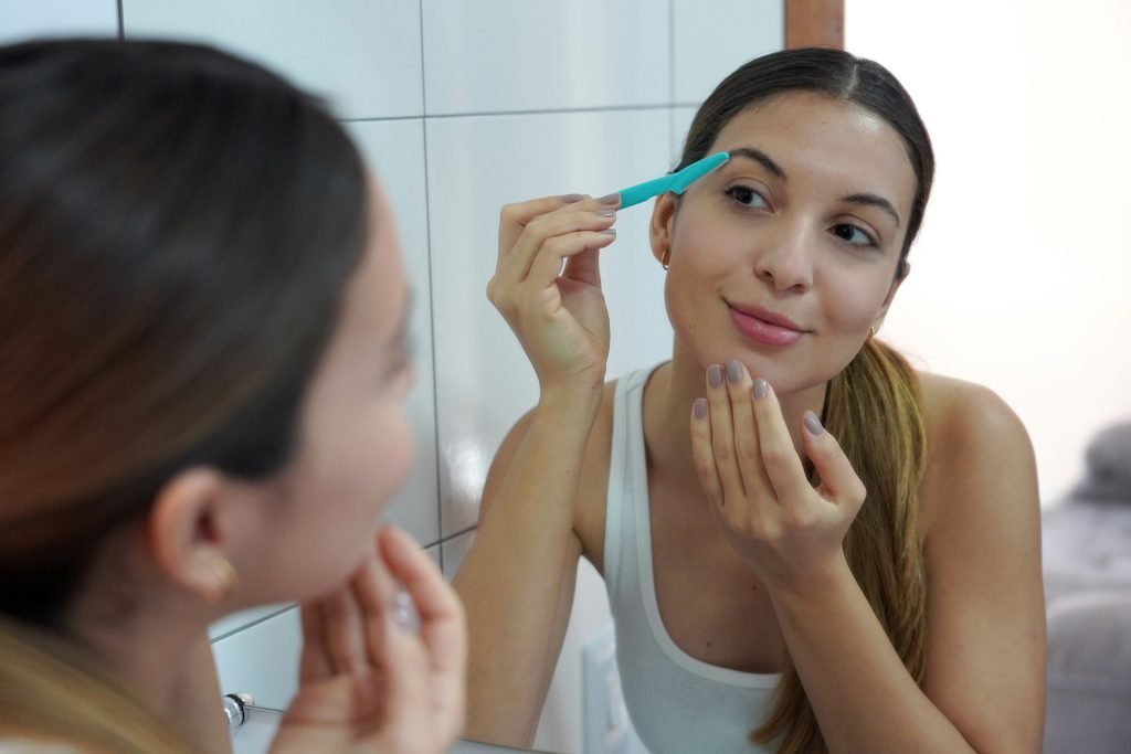  Epilazione del viso con dermaplaning Primo piano di una bellissima giovane donna che si rade il viso con un rasoio a casa. Concetto di dermaplaning pro e contro 