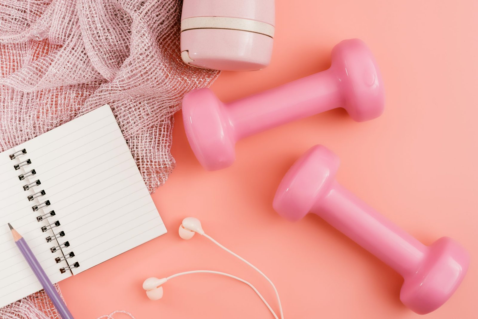 Fotografia stock di attrezzi da fitness, manubri, blocco note, matita e auricolari su sfondo rosa. concetto di motivazione per sport