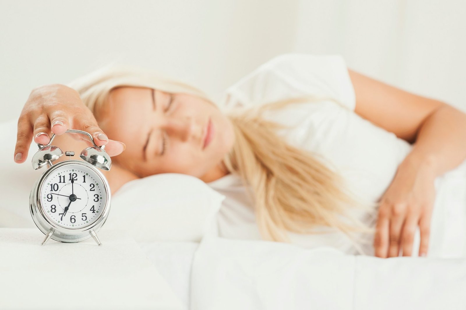 donna a letto che riposa e allunga la mano per spegnere la sveglia - concetto Dormire poco rischi