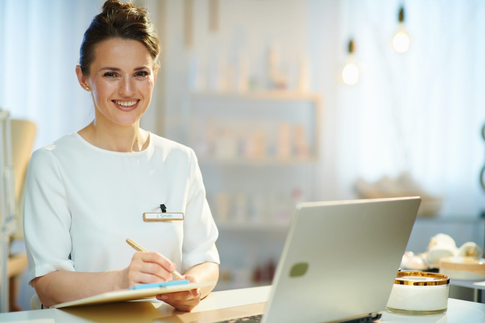 etstetista sorridente con blocco appunti e computer portatile in un moderno salone di bellezza.