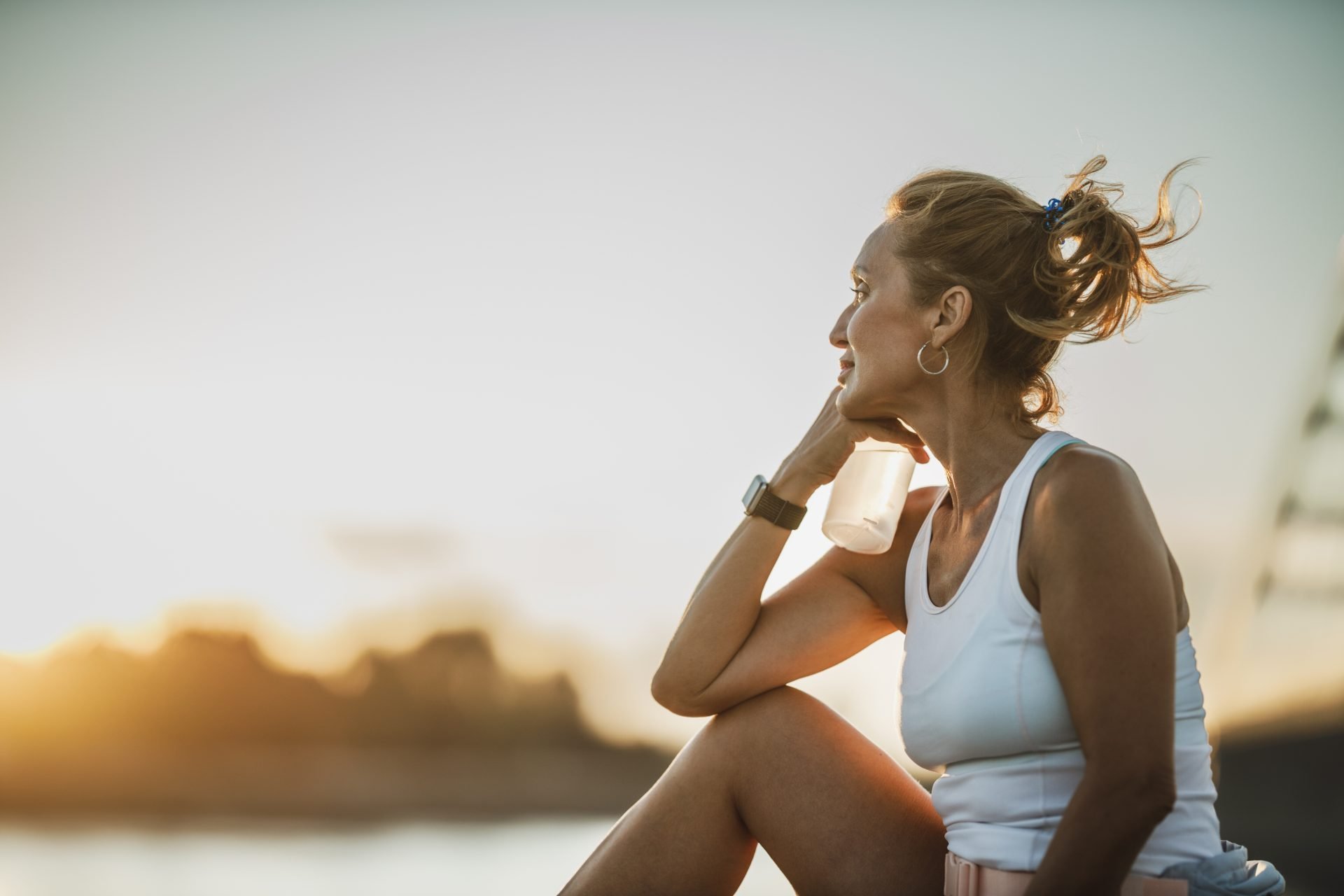 Una sportiva di mezza età è seduta vicino al fiume, pensierosa, e guarda in lontananza mentre si riposa dopo l'allenamento.Concetto quale tipo di magnesio assumere in menopausa 