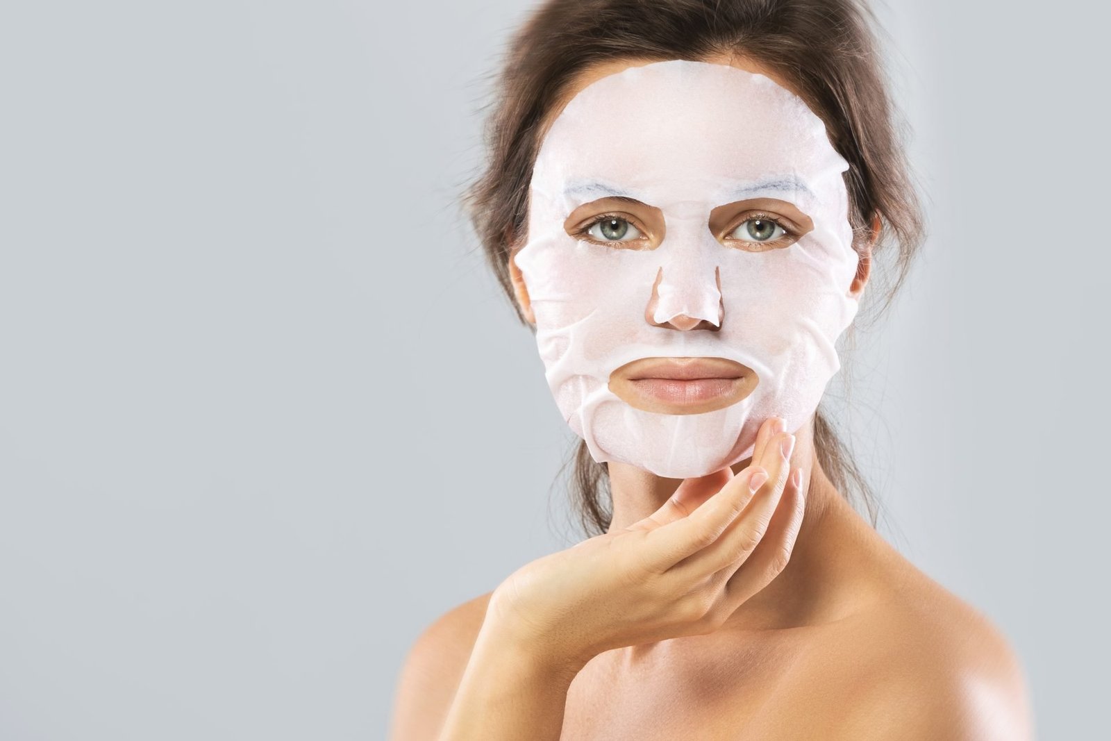 Trattamenti di bellezza e cura del viso. Donna con una maschera idratante in fogli sul viso, isolata su sfondo grigio. Concetto maschere in tessuto funzionano