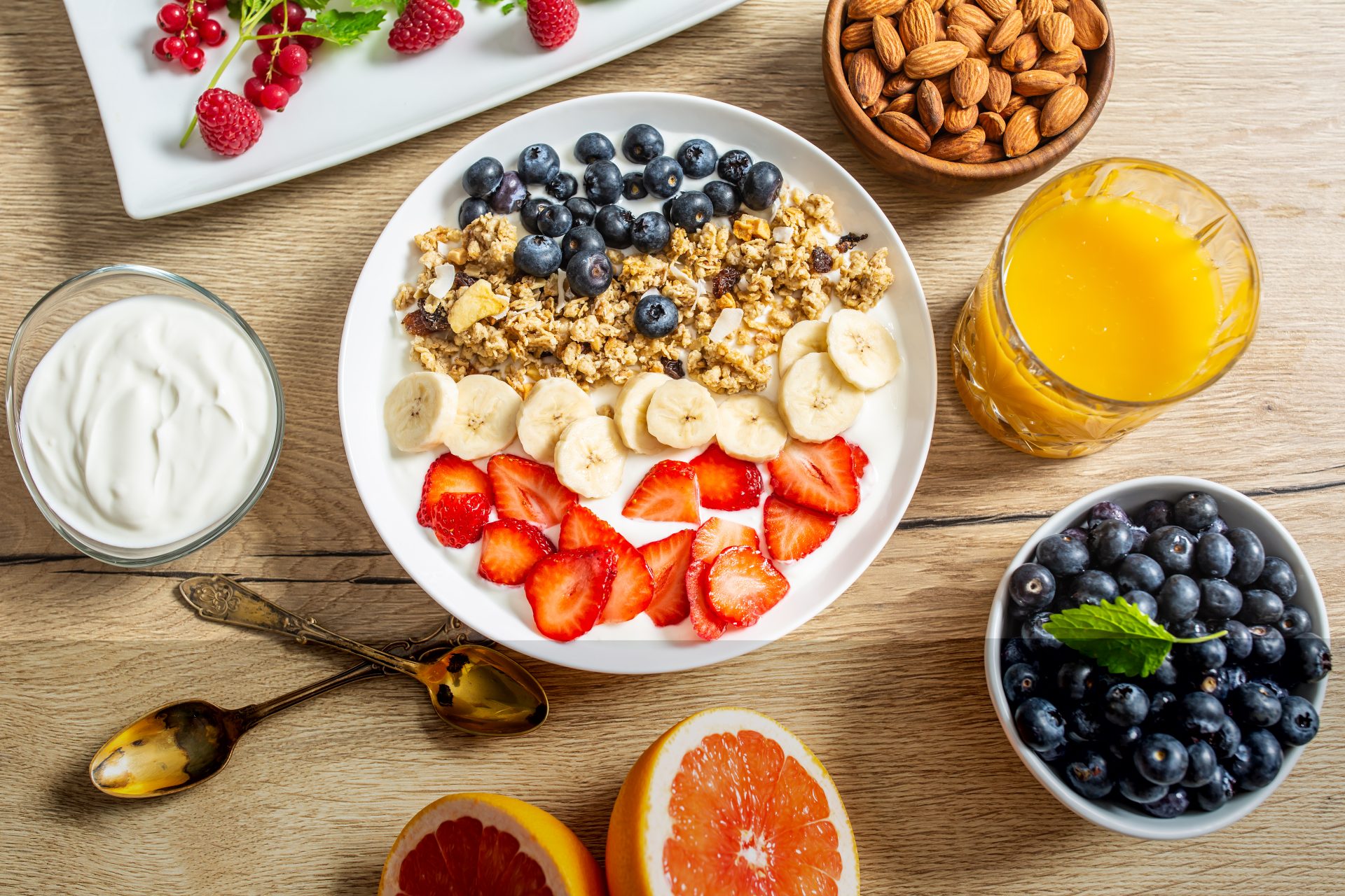 COLAZIONE IDEALE IN MENOPAUSA : Colazione sana servita con yogurt, muesli, mirtilli, fragole e banana. Granola, mandorle, frutti di bosco, succo di agrumi ed erbe aromatiche.