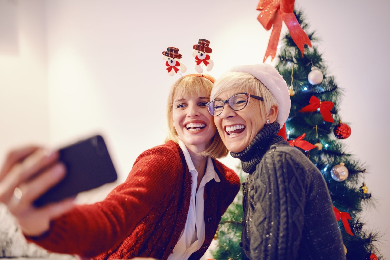 Una graziosa donna e sua madre si scattano un selfie davanti all'albero di Natale decorato. Periodo natalizio. Regali di natale beauty per la mamma 