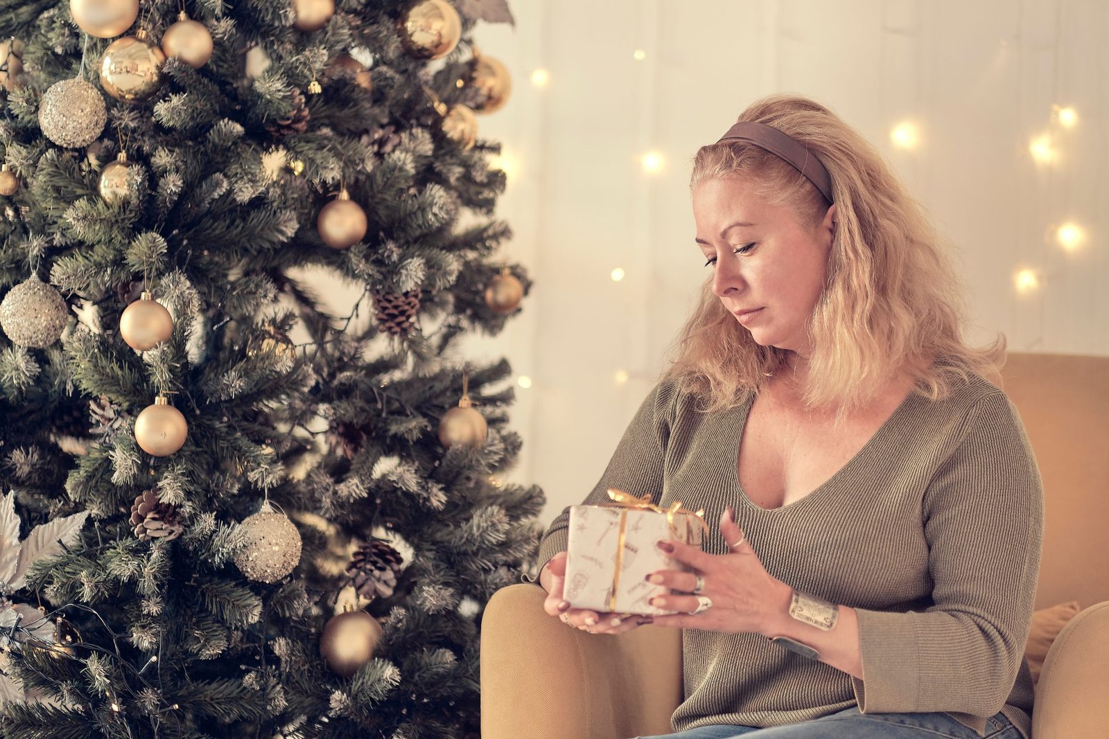 regali di natale beauty per la mamma - Donna matura che riflette accanto all'albero di Natale seduta su un divano in soggiorno.
