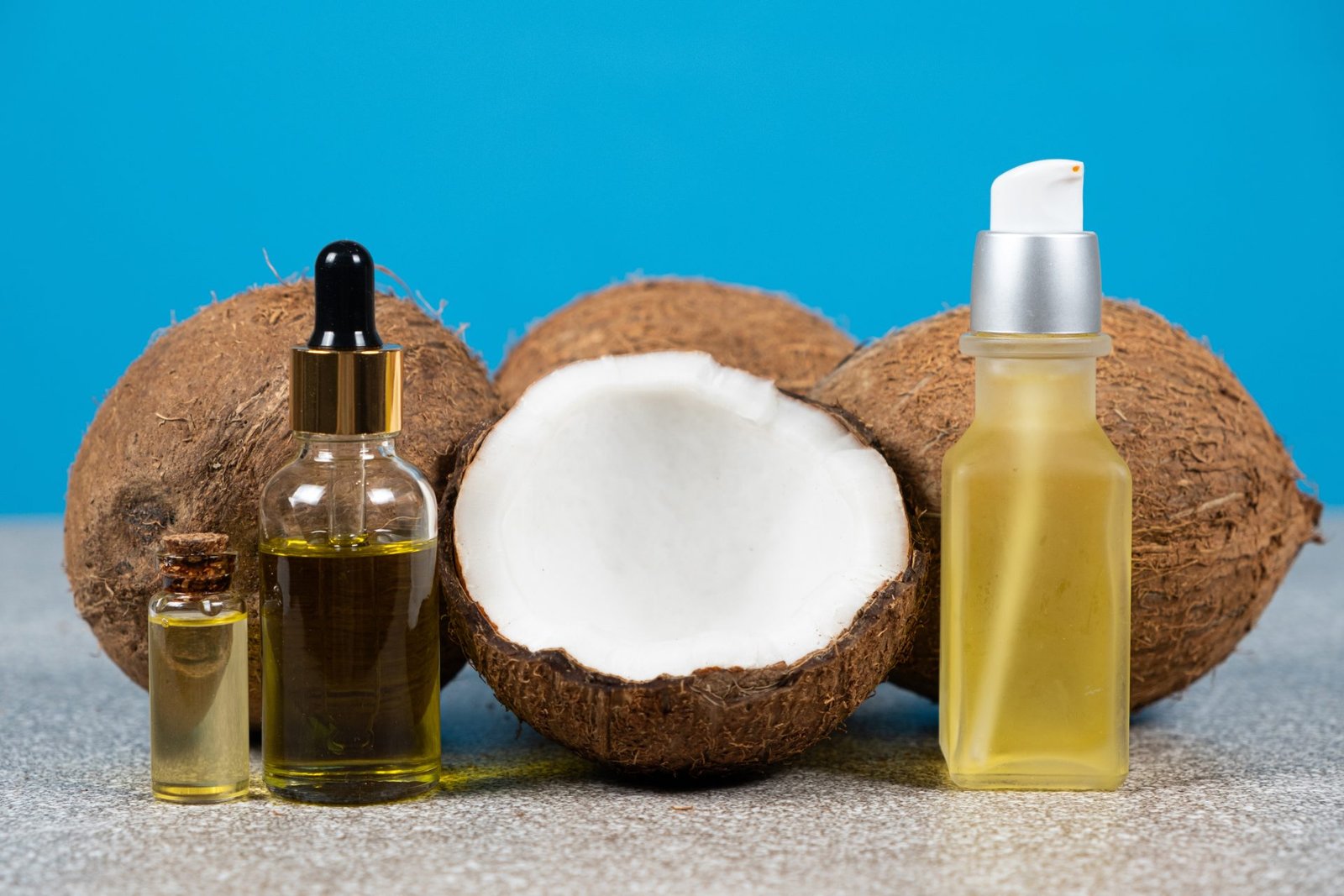 Olio di cocco in bottiglie di vetro e noci di cocco su sfondo blu- concetto olio di cocco per capelli come usarlo