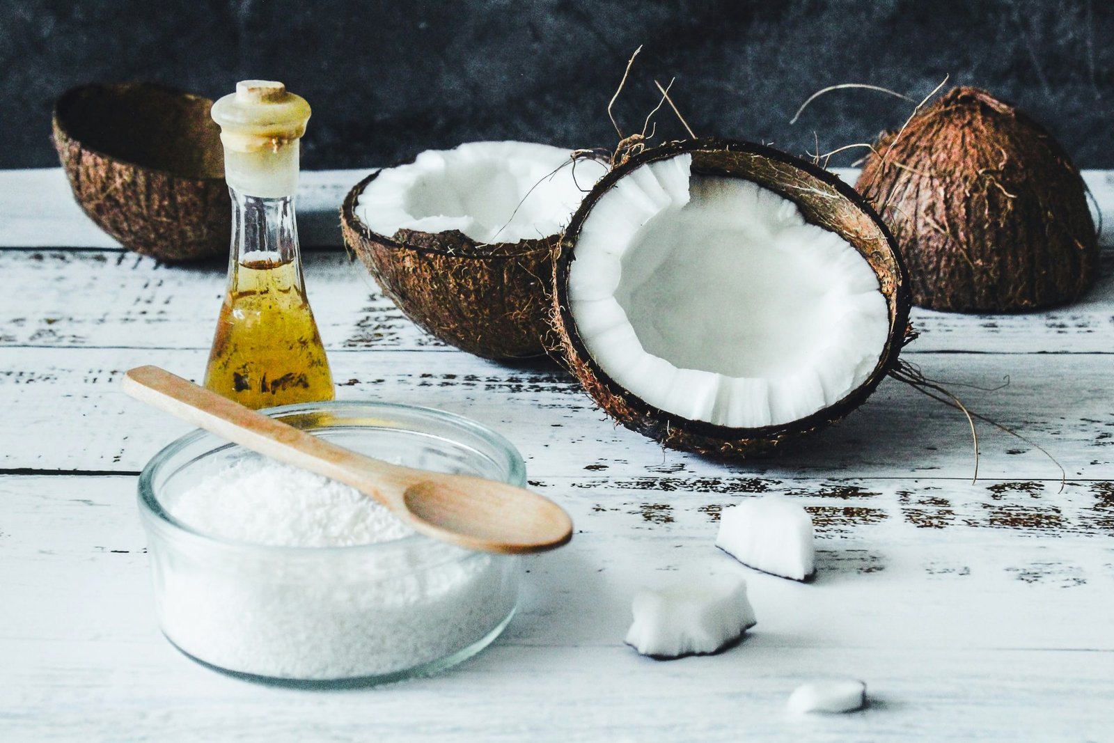 Olio di cocco in bottiglia di vetro , cocco rapè in ciotola con cucchiaio di legno e noci di cocco su legno chiaro bianco- concetto olio di cocco come usarlo