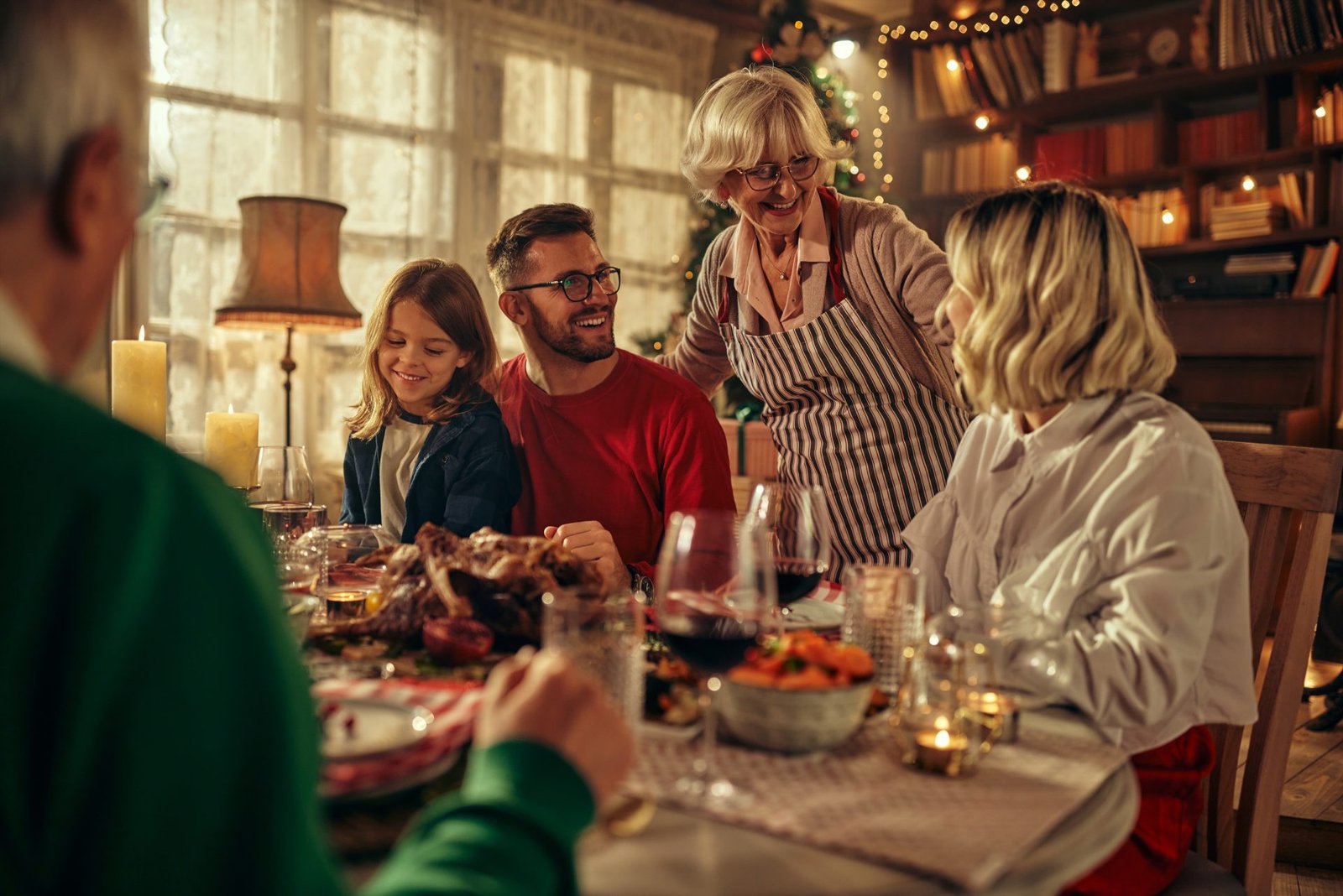 Una famiglia di tre generazioni seduta a tavola durante il periodo natalizio, che trascorre del tempo di qualità insieme. Un bambino in età prescolare con genitori e nonni si gode il Natale a casa, gustando del cibo delizioso. Concetto illustrato come non ingrassare durante le feste 