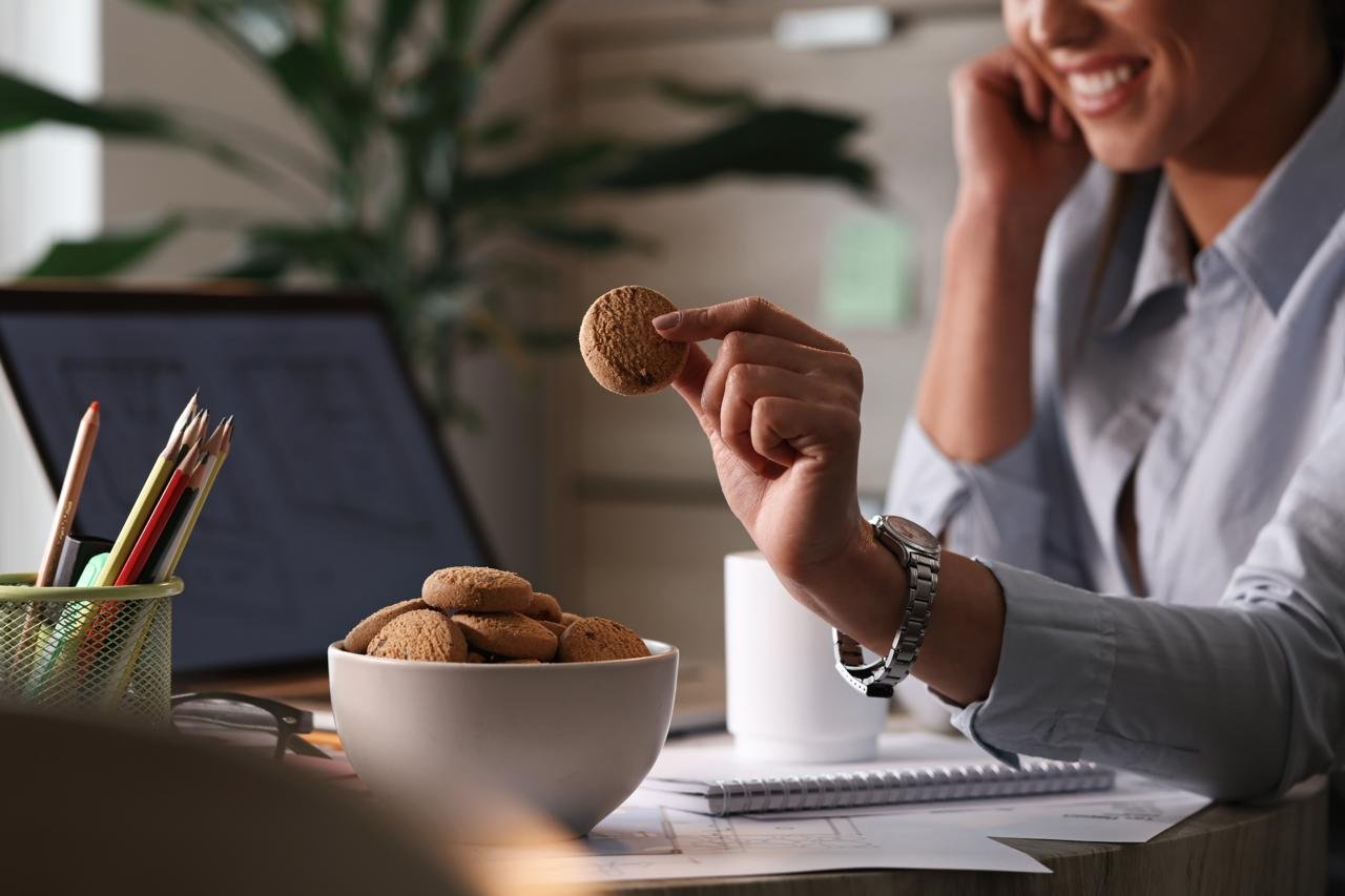 donna che fa spuntino con biscotti mentre lavora alla scrivania col il pc. Concetto come non ingrassare durante le feste