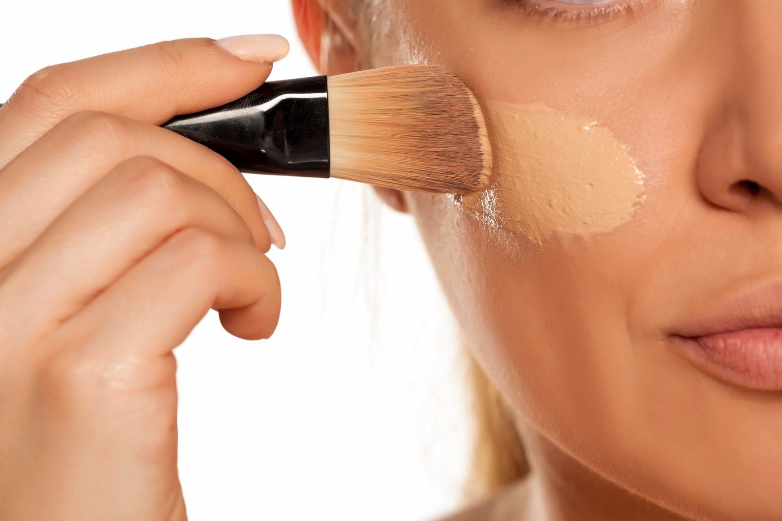 PRIMO PIANO DI DONNA CHE APPLICA IL FONDOTINTA SULLA PELLE CON UN PENNELLO DA TRUCCO. TEMA MIGLIORI FONDOTINTA LOW COST 2026 